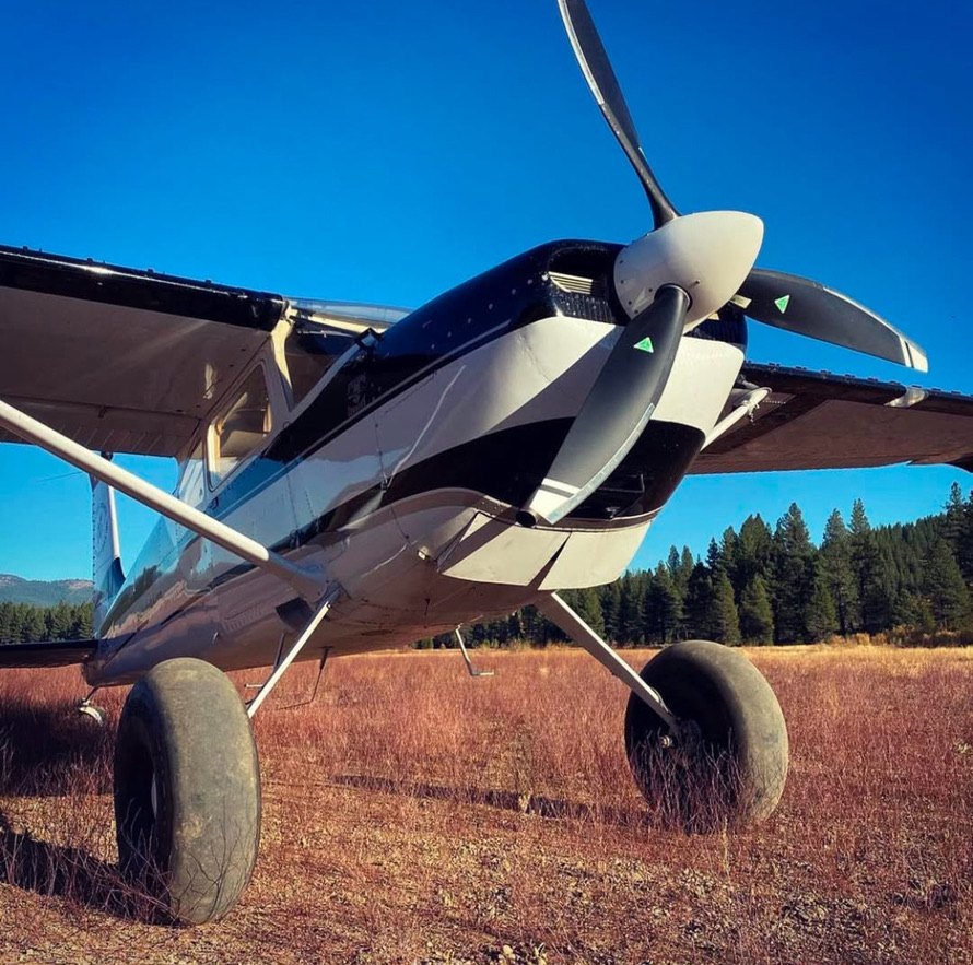 Cessna with a black and white three-blade MT propeller on a grass strip under blue sky