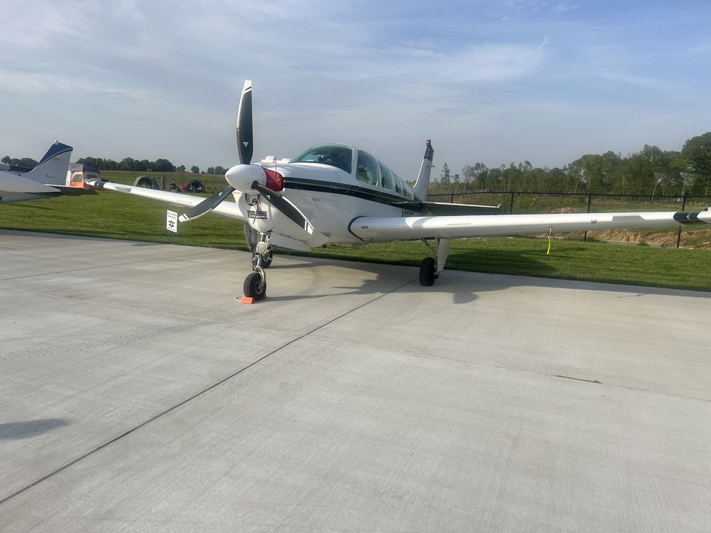 White Beechcraft Bonanza parked on a concrete ramp with a black MT propeller