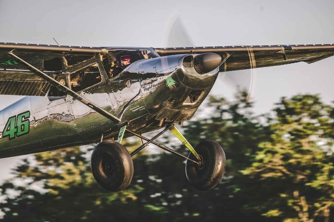 Polished Cessna 185 with green number 46 landing, MT propeller blurred