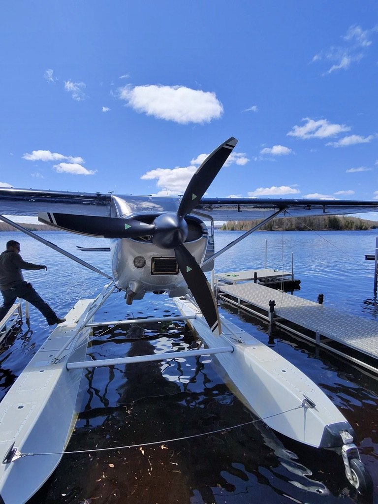 Silver floatplane on floats at a dock with a black three-blade MT propeller