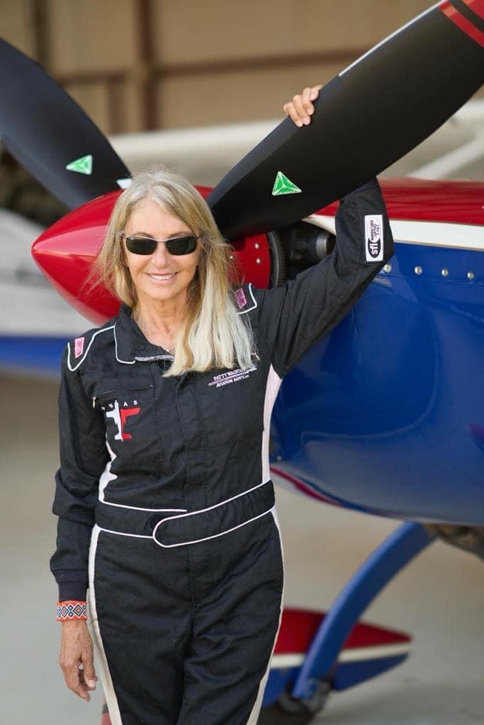 Smiling woman in a black flight suit holding a black three-blade MT propeller