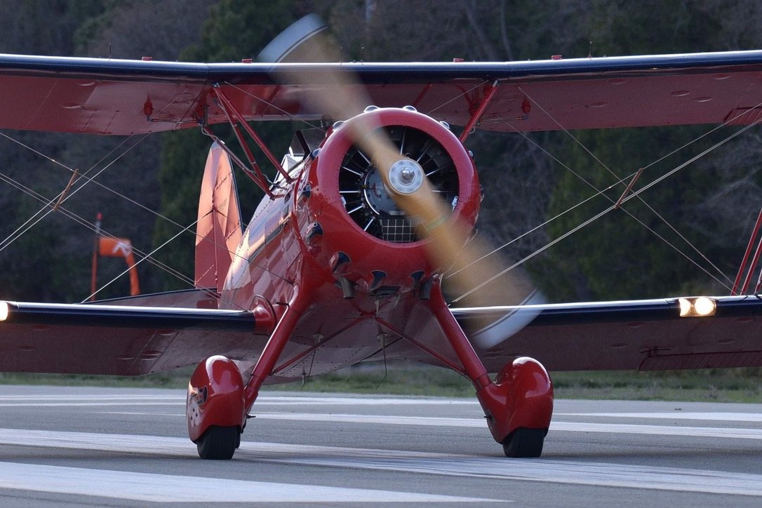 Red Waco biplane taxiing with a wooden MT propeller spinning
