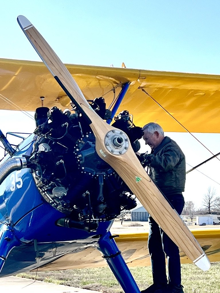 Man working on the radial engine of a blue and yellow Stearman biplane with a wooden MT propeller