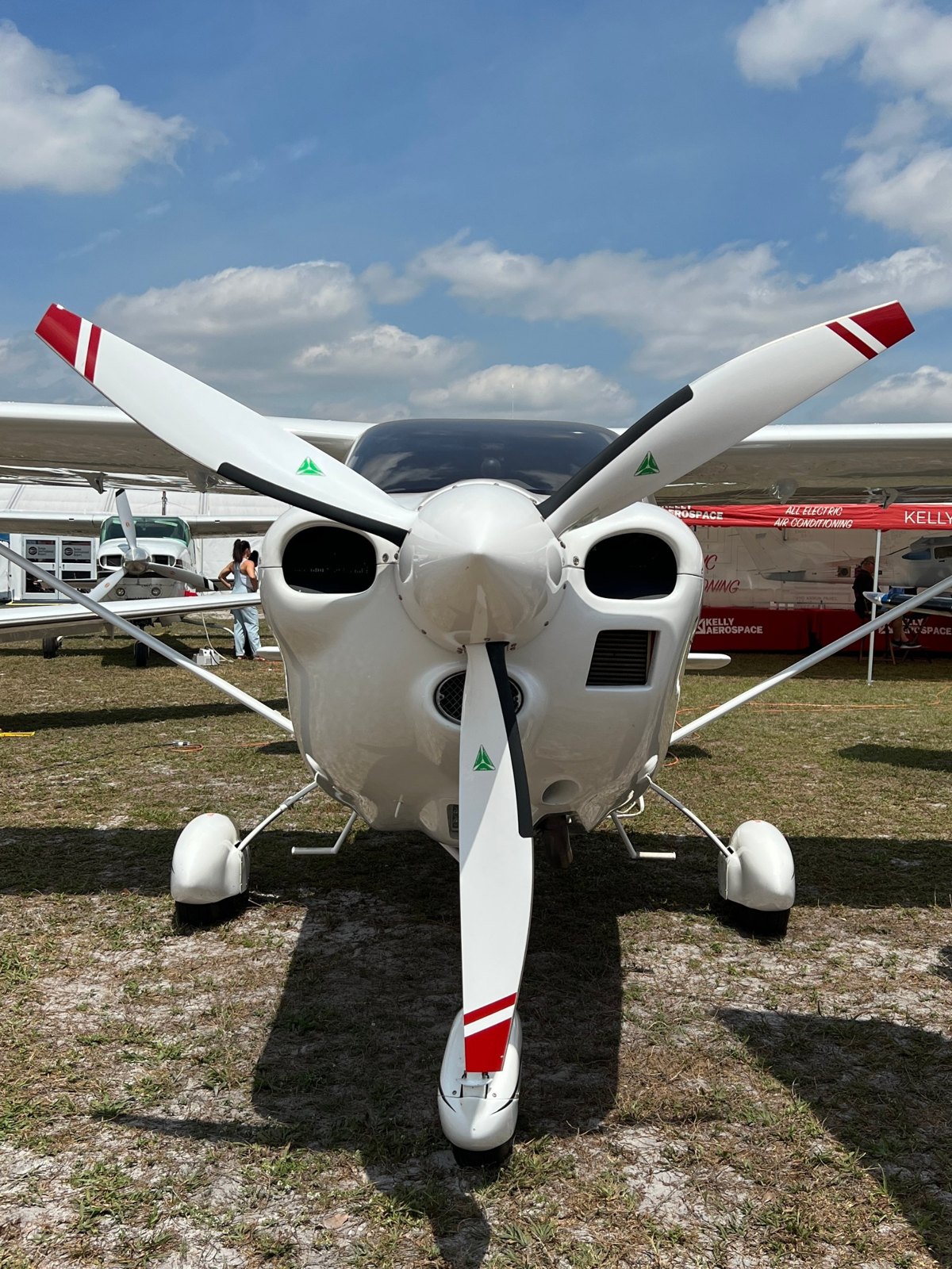 White single-engine aircraft with a white three-blade MT propeller with red tips on a grass field