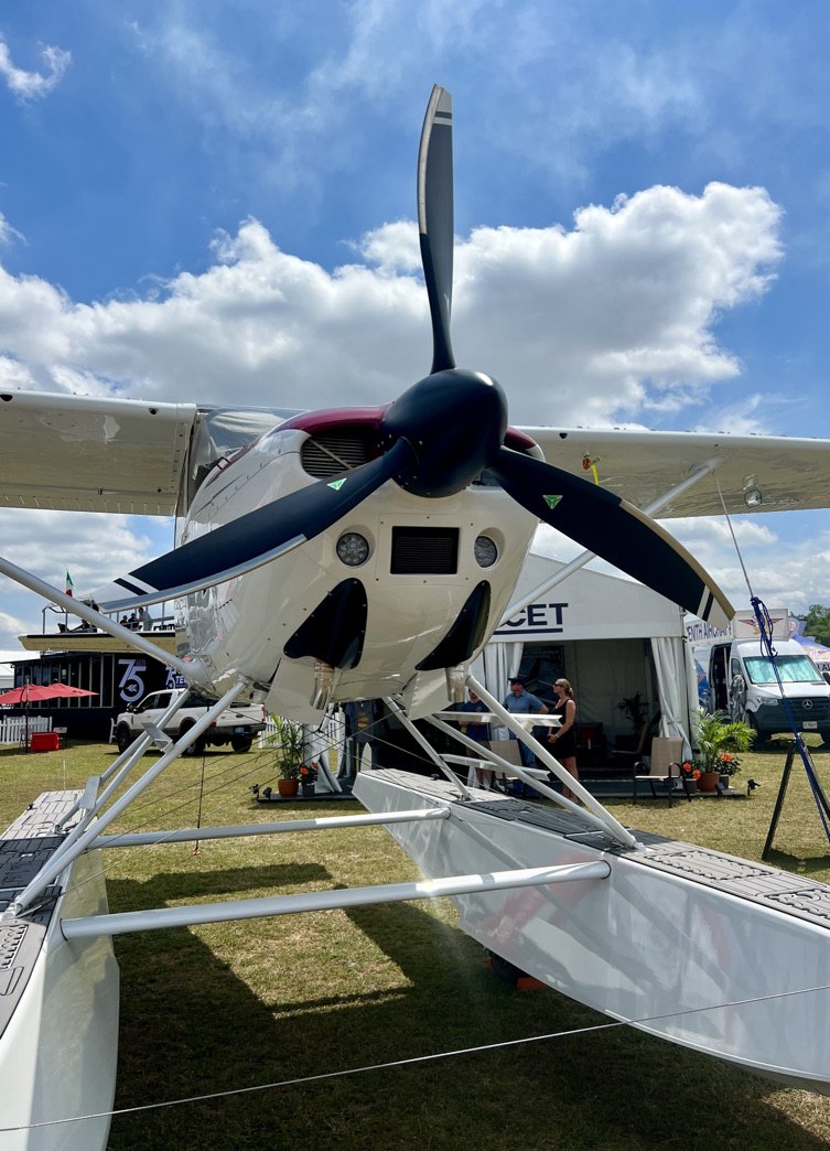 Floatplane on grass at an airshow with a black three-blade MT propeller