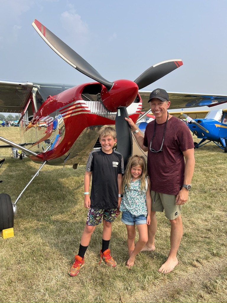 A man and two children standing in front of a red polished Cessna with a black MT propeller