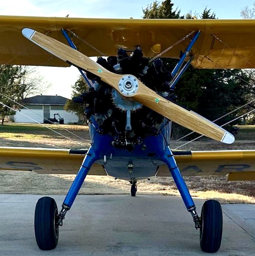 Blue and yellow Stearman biplane from the front with a wooden MT propeller