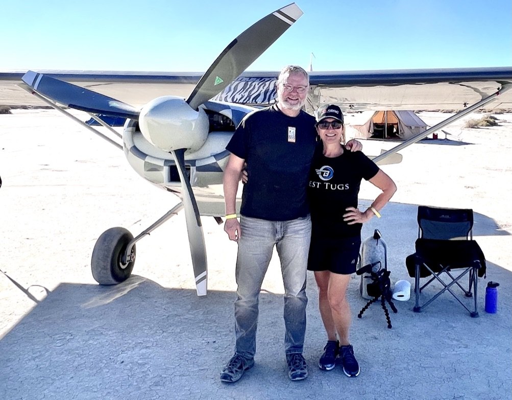 A man and a woman standing in front of a bush plane on a dry lakebed