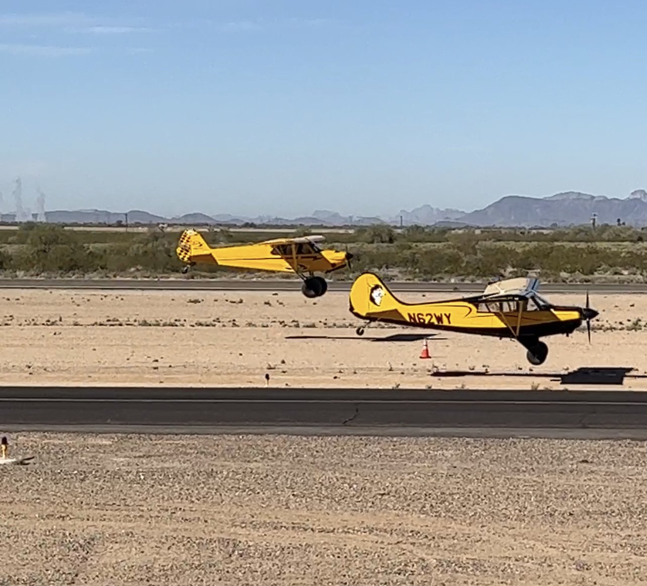 Two yellow Cubs taking off side by side from a desert airstrip