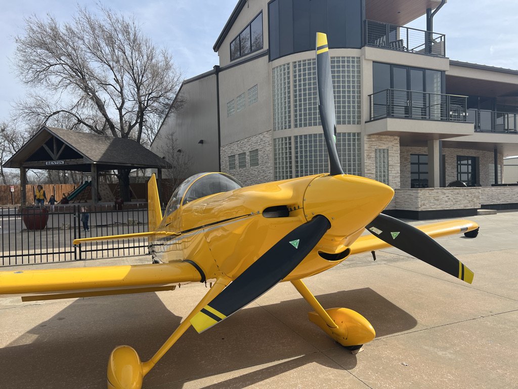 Yellow race plane with a black MT propeller parked outside a restaurant