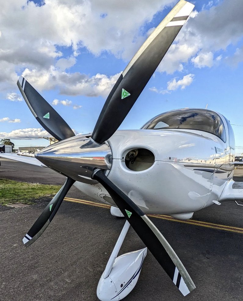 Chrome-spinner Cirrus with a black four-blade MT propeller under a blue sky with clouds