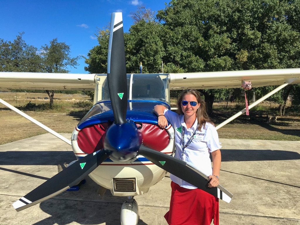 Smiling woman in sunglasses leaning on a black MT propeller in front of a Cessna