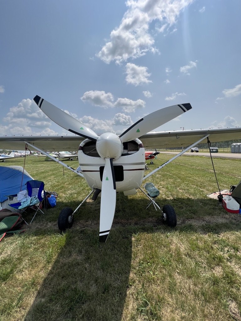 White Cessna from the front with a white three-blade MT propeller on a grass field