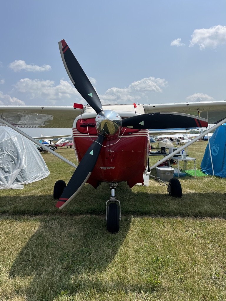 Red Cessna with a black three-blade MT propeller and chrome spinner on a grass field