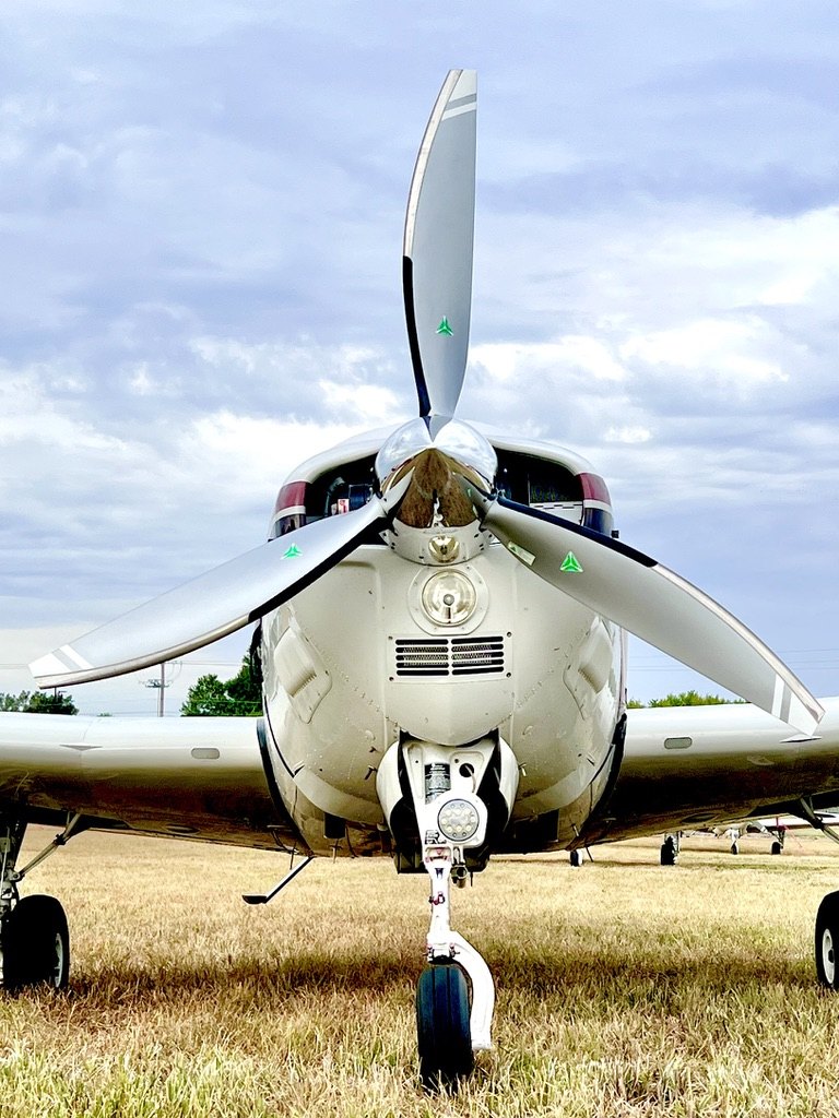 Front view of a Beechcraft with a three-blade MT propeller and chrome spinner on a grass field