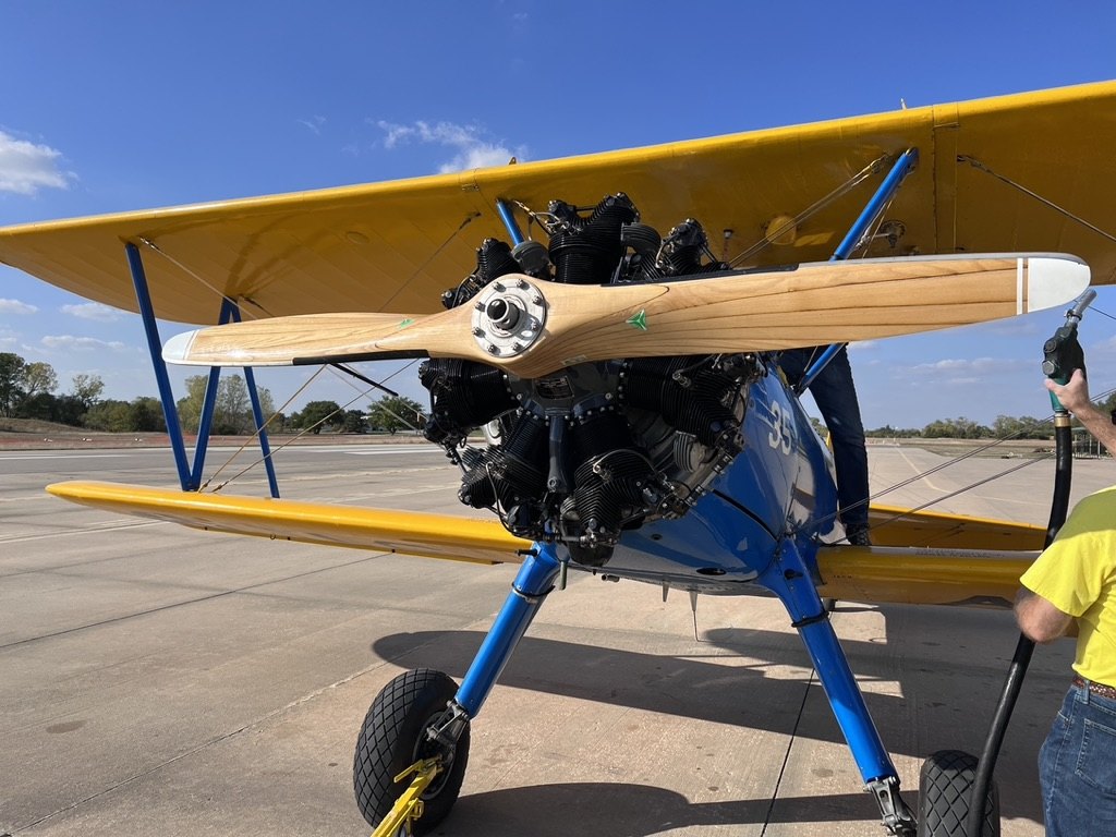 Front view of a blue and yellow Stearman biplane being fueled with a wooden MT propeller