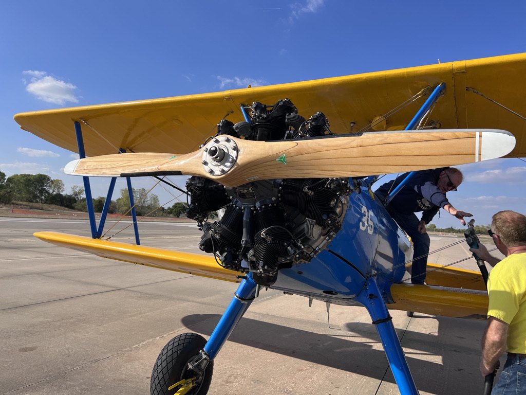 Blue and yellow Stearman biplane being fueled with a wooden MT propeller on the ramp