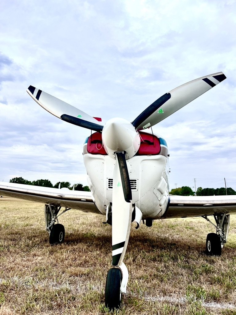 Front view of a white Beechcraft with a three-blade MT propeller on a grass field