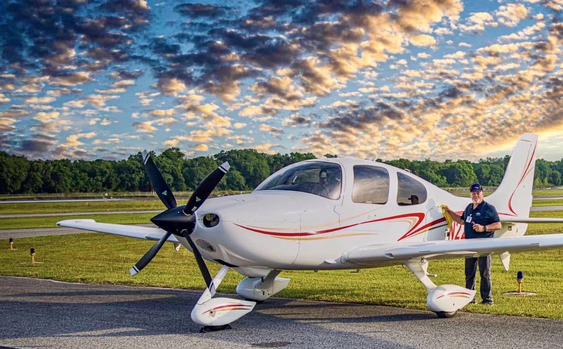 White Cirrus with a black four-blade MT propeller at sunrise, with a man cleaning the wing