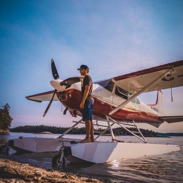 Man standing on the float of a red and white Cessna 185 floatplane with a black three-blade MT propeller