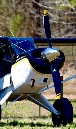 Close view of a navy and yellow bush plane with a black two-blade MT propeller on grass