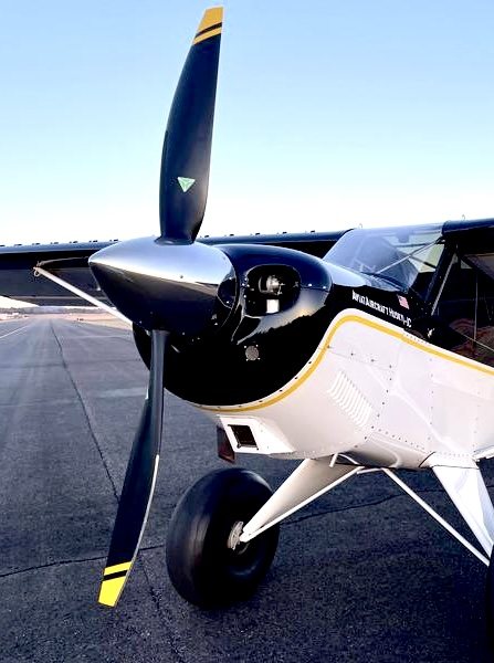 Black and white Aviat Husky on a taxiway with a black two-blade MT propeller with yellow tips