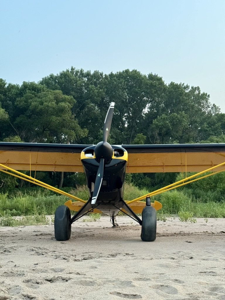 Black and yellow bush plane on a sandy riverbank with a black two-blade MT propeller