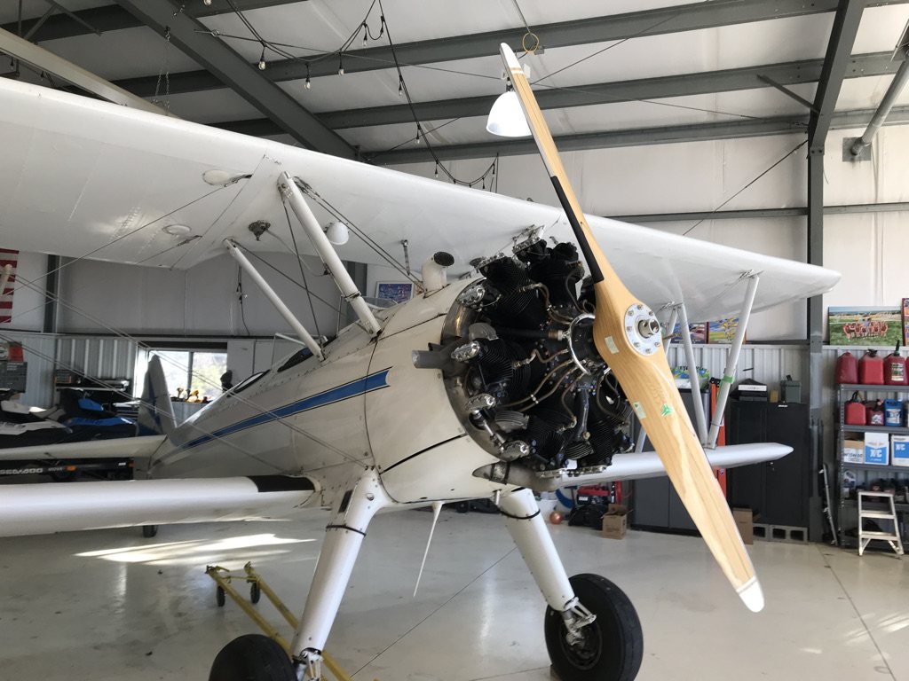 White Stearman biplane in a hangar with a wooden MT propeller