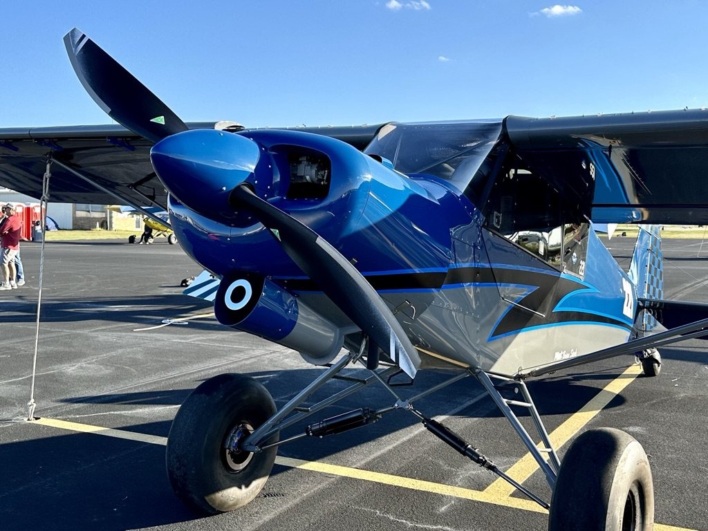 Blue and black bush plane with a black MT propeller and large tires on a ramp
