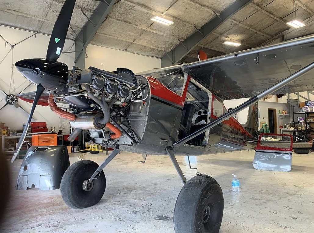 Cessna 180 with its engine cowling open in a hangar and a black MT propeller attached