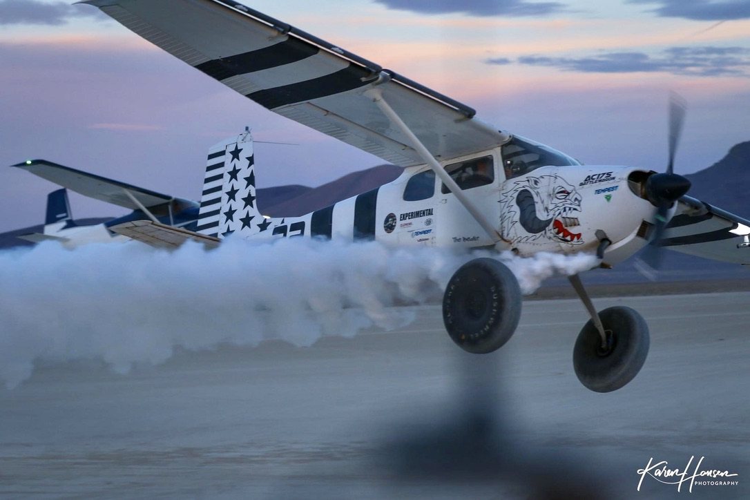 White and black Cessna taking off in a cloud of dust at dusk with a black MT propeller