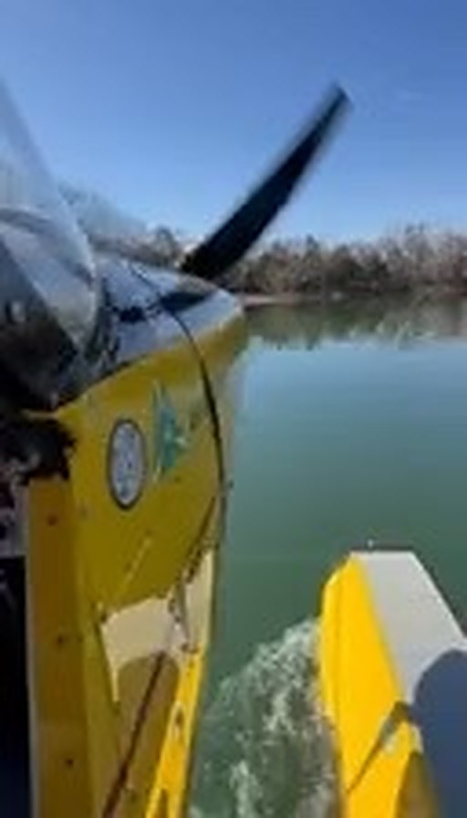 Yellow floatplane with a black MT propeller seen from the cockpit side, over water