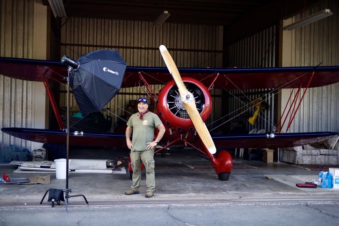 Juan Brown standing in front of his red Waco YMF-5 biplane in a hangar