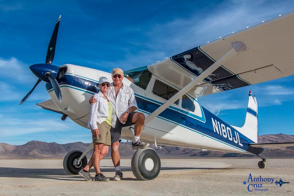 Cessna 180 with a three-blade MT propeller on a dry lakebed, with two people